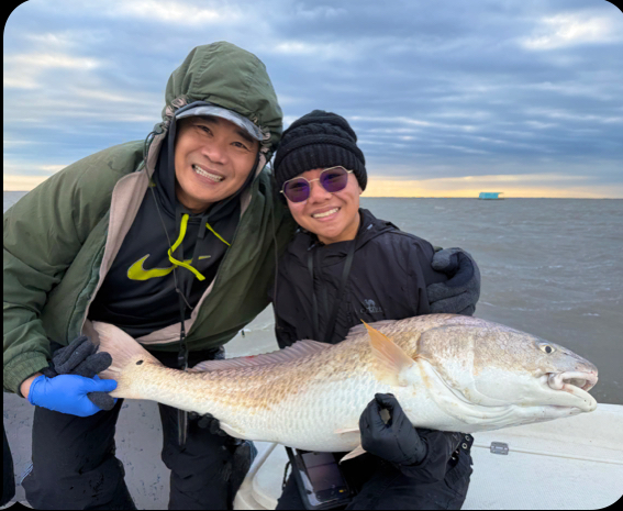 Two smiling anglers holding a large redfish aboard the boat